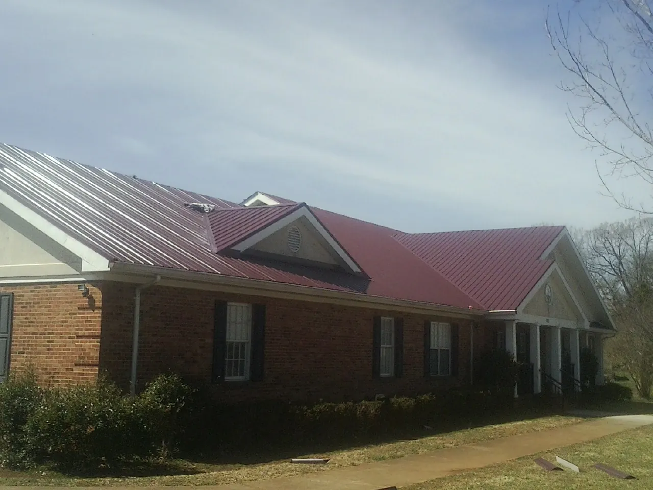 Red metal roof with gabled entries on a long brick building, from a Hail Damage Roof Repair job in The Plains