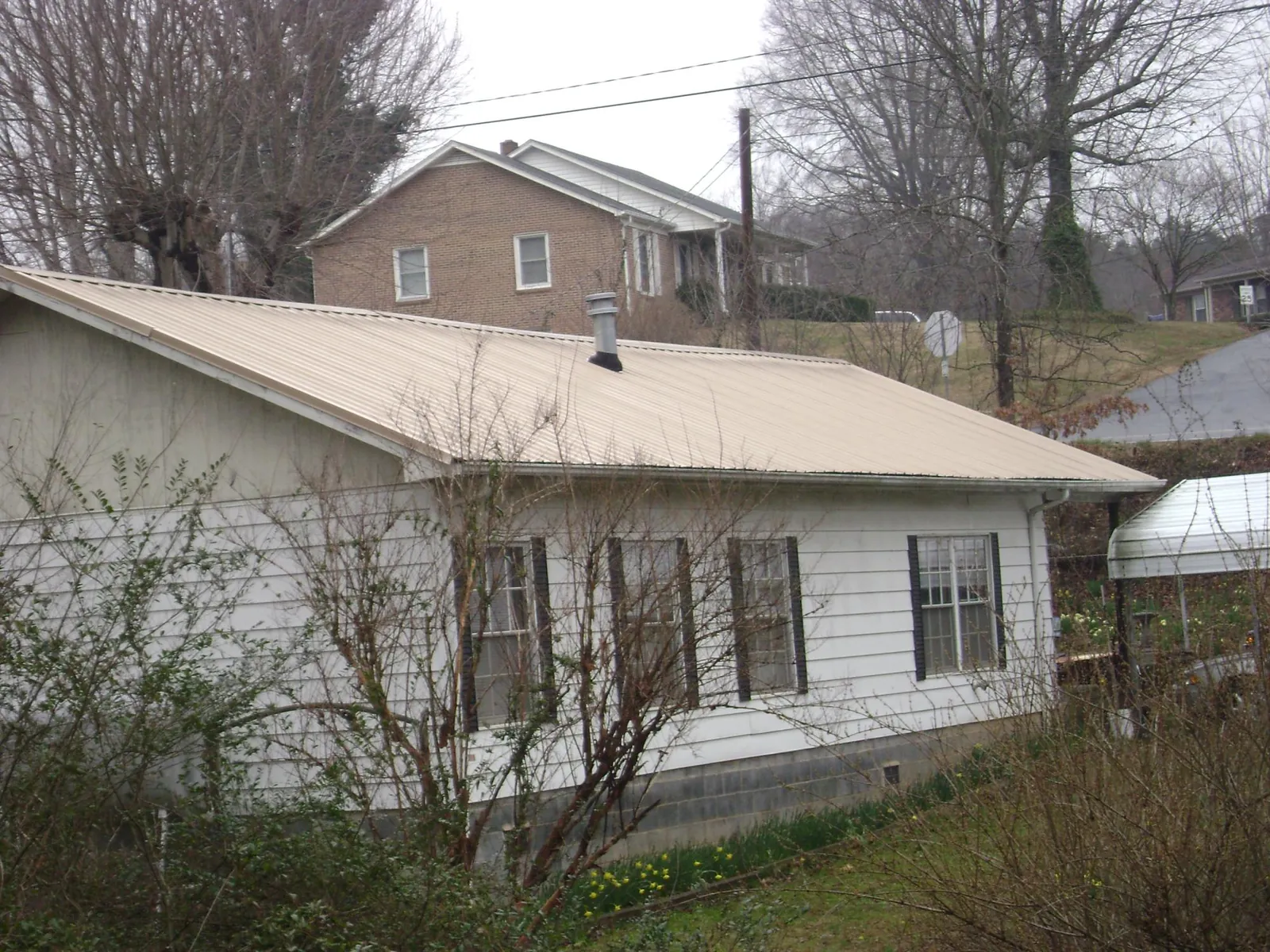 Tan metal roof on a white sided house set into a hillside — Commercial Roofing by Roofing Brothers in The Plains